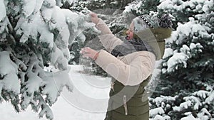Happy child girl plays with snowy fir tree branches, winter forest, beautiful landscape