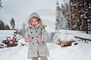 Happy child girl plays in winter snowy forest with tree felling on background