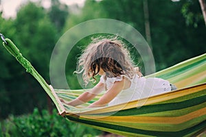 Happy child girl relaxing in hammock on summer camp in forest. Outdoor seasonal activities