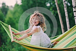 Happy child girl relaxing in hammock on summer camp in forest. Outdoor seasonal activities