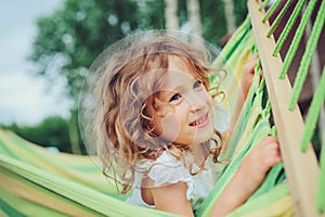 Happy child girl relaxing in hammock on summer camp in forest. Outdoor seasonal activities