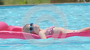 Happy child girl relaxing on inflatable air mattress in swimming pool on sunny summer day during tropical vacations