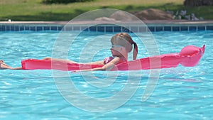 Happy child girl relaxing on inflatable air mattress in swimming pool on sunny summer day during tropical vacations