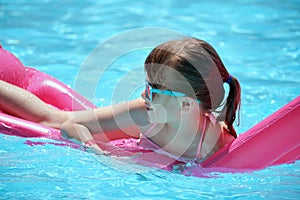 Happy child girl relaxing on inflatable air mattress in swimming pool on sunny summer day during tropical vacations