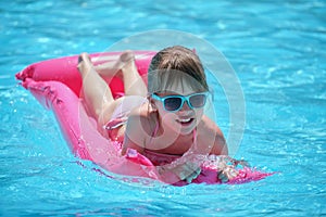 Happy child girl relaxing on inflatable air mattress in swimming pool on sunny summer day during tropical vacations