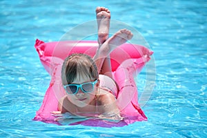 Happy child girl relaxing on inflatable air mattress in swimming pool on sunny summer day during tropical vacations