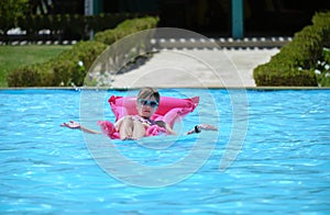 Happy child girl relaxing on inflatable air mattress in swimming pool on sunny summer day during tropical vacations