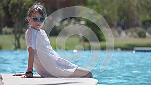 Happy child girl relaxing on swimming pool side on sunny summer day