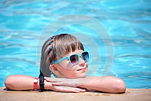 Happy child girl relaxing on swimming pool side on sunny summer day