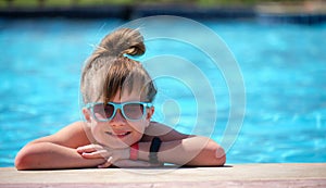 Happy child girl relaxing on swimming pool side on sunny summer day