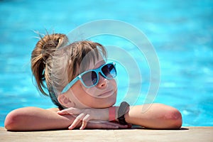 Happy child girl relaxing on swimming pool side on sunny summer day