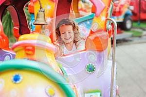 Happy child girl riding train on funfair on summer vacation