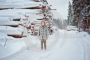 Happy child girl on the road in winter snowy forest with tree felling on background