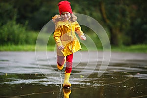 Happy child girl with rubber boots runs in puddle on autumn wal