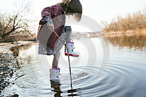 Happy child girl in rubber unicorn boots running and jumping in puddles in spring