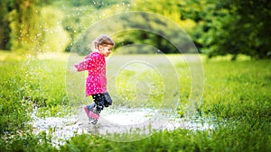 Happy child girl running and jumping in puddles after rain