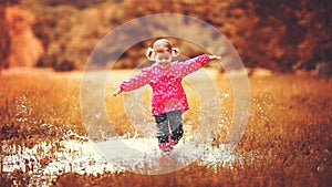 Happy child girl running and jumping in puddles after rain