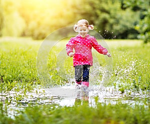 Happy child girl running and jumping in puddles after rain