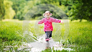 Happy child girl running and jumping in puddles after rain