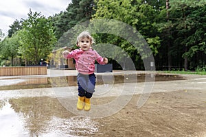 happy child girl running and jumping in puddles after rain in summer