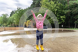 happy child girl running and jumping in puddles after rain in summer