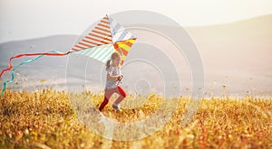Happy child girl running with kite at sunset outdoors