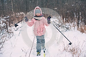 happy child girl skiing in winter snowy forest, spending holidays outdoor.