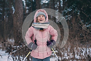 Happy child girl skiing in winter snowy forest, spending holidays outdoor.