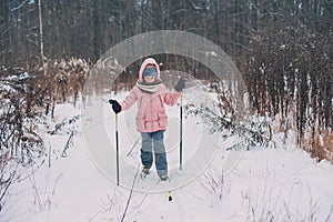 Happy child girl skiing in winter snowy forest, spending holidays outdoor.