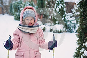 Happy child girl skiing in winter snowy forest, spending holidays outdoor.