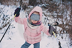 Happy child girl skiing in winter snowy forest, spending holidays outdoor.