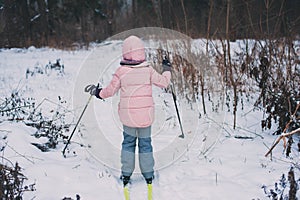 Happy child girl skiing in winter snowy forest, spending holidays outdoor.