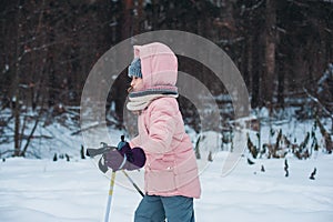 Happy child girl skiing in winter snowy forest, spending holidays outdoor.