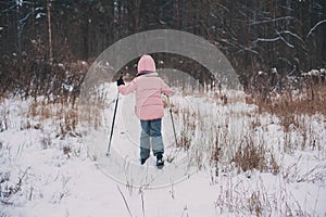 Happy child girl skiing in winter snowy forest, spending holidays outdoor.