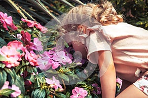 Happy child girl smells beautiful flowers in blossoming summer park concept love nature lifestyle