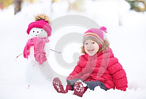 Happy child girl with a snowman on a winter walk