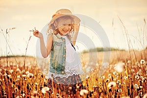 Happy child girl in straw playing with blow balls on summer field
