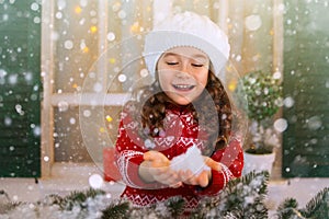 Happy child girl stretches her hand to catch falling snowflakes.