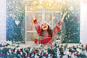 Happy child girl stretches her hand to catch falling snowflakes.