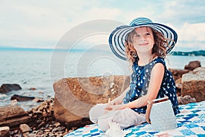 Happy child girl in stripe hat playing on the beach and listen to sea shell