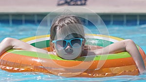 Happy child girl swimming on inflatable circle in swimming pool on sunny summer day during tropical vacations