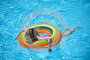 Happy child girl swimming on inflatable circle in swimming pool on sunny summer day during tropical vacations