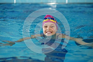 Happy child girl swims in swimming pool. Swim cap and goggles. Training and sports concept