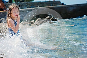 Happy child girl in swimsuit relaxing on the beach and playing with water. Summer vacation at sea.