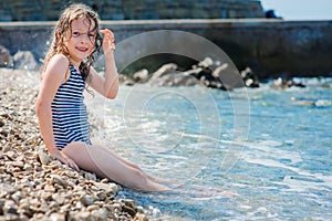 Happy child girl in swimsuit relaxing on the beach and playing with water. Summer vacation at sea.