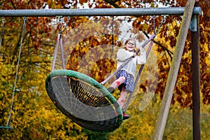 Happy child girl on swing in fall. Little kid playing in the autumn on playground, swinging and having fun. Autumnal