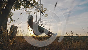 Happy child girl on swing at golden summer sunset. Silhouette of a young teenager girl swinging on the lone tree at