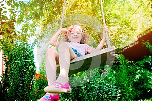 Happy child girl on swing in sunny summer garden
