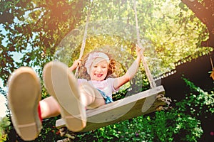 Happy child girl on swing in sunny summer garden