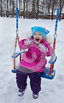 Happy child girl on swing in sunset winter. Little kid playing on a winter walk in nature